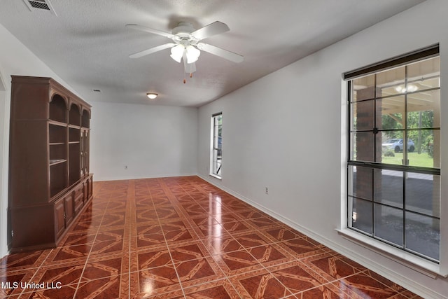 unfurnished room featuring dark tile patterned floors, ceiling fan, a textured ceiling, and visible vents