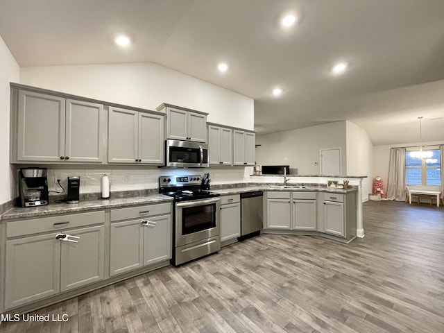 kitchen with vaulted ceiling, decorative backsplash, light wood-type flooring, kitchen peninsula, and stainless steel appliances