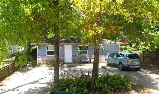 view of property hidden behind natural elements featuring brick siding and fence