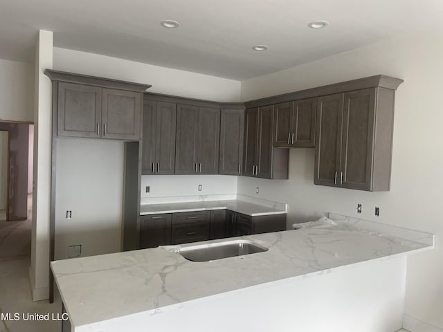 kitchen featuring recessed lighting, a sink, dark brown cabinetry, and light stone countertops