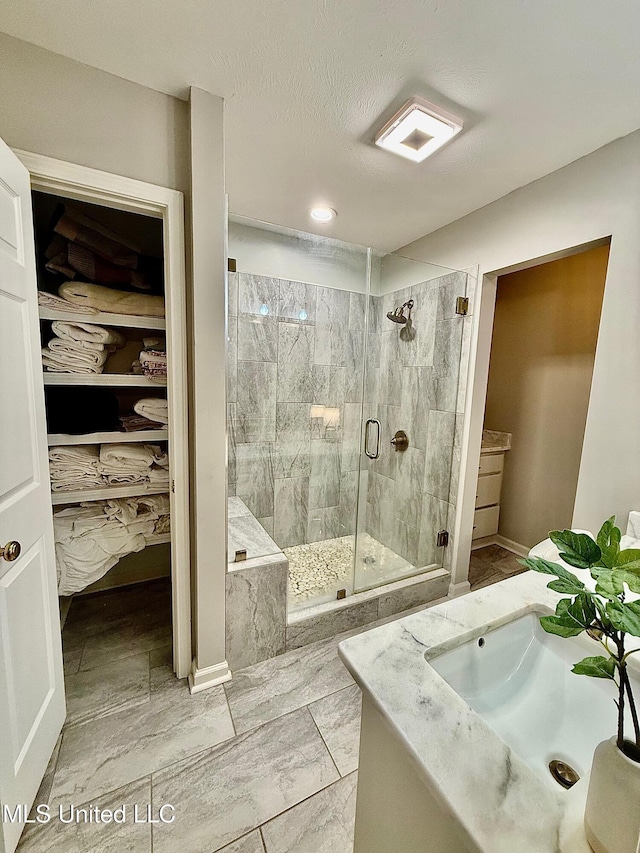 full bathroom with vanity, a walk in closet, marble finish floor, and a stall shower
