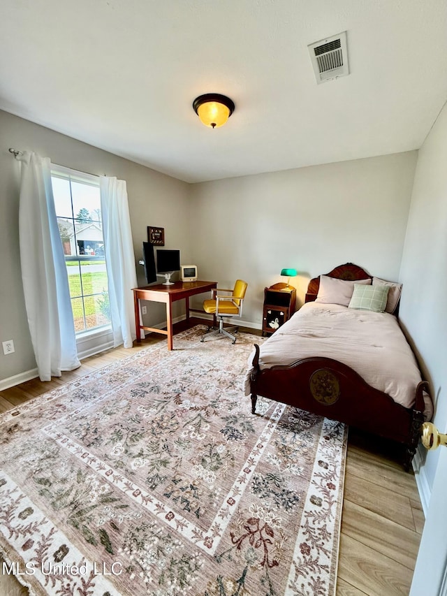 bedroom with baseboards, visible vents, and wood finished floors