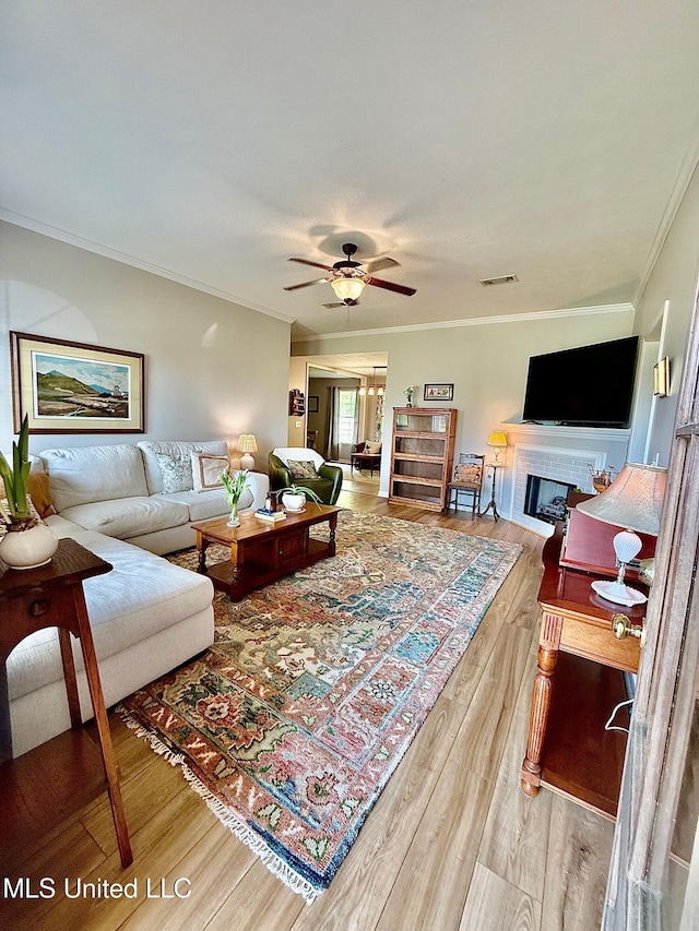 living room featuring crown molding, ceiling fan, a fireplace, wood finished floors, and visible vents