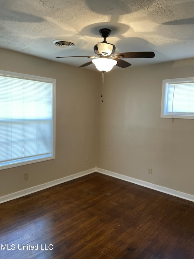 empty room with dark wood-type flooring, baseboards, visible vents, and a textured ceiling