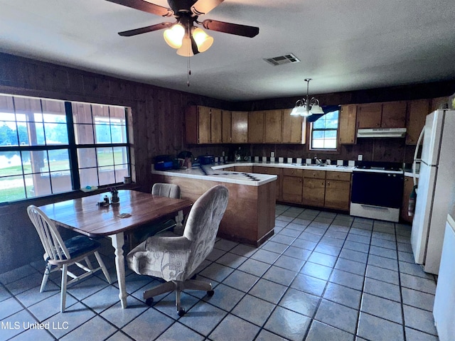 kitchen featuring white appliances, ceiling fan with notable chandelier, kitchen peninsula, hanging light fixtures, and light tile patterned floors