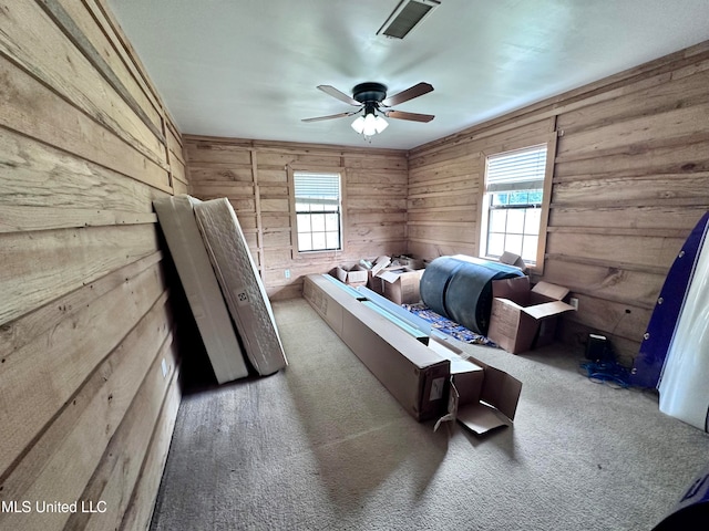 carpeted bedroom featuring wood walls, multiple windows, and ceiling fan