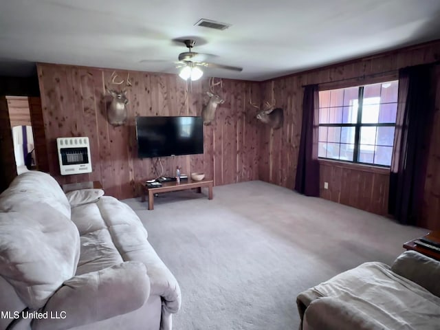 carpeted living room featuring wooden walls, heating unit, and ceiling fan