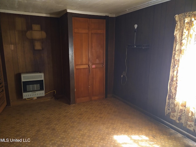 unfurnished bedroom with heating unit, a closet, and wood walls