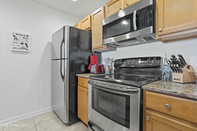 kitchen with appliances with stainless steel finishes, stone countertops, light tile patterned flooring, and baseboards