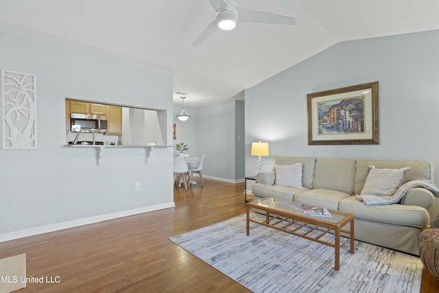 living area featuring lofted ceiling, baseboards, ceiling fan, and light wood finished floors