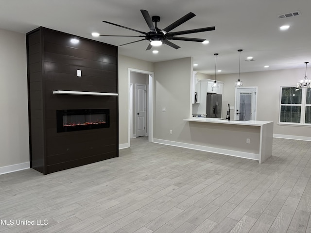 kitchen with pendant lighting, white cabinets, light hardwood / wood-style flooring, a large fireplace, and stainless steel fridge with ice dispenser