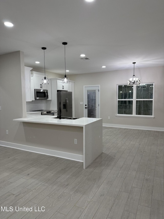 kitchen with white cabinets, stainless steel appliances, decorative light fixtures, and light hardwood / wood-style floors