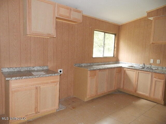 kitchen with light tile patterned flooring, light brown cabinets, wood walls, and sink