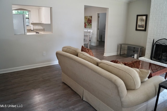 living room with dark wood-type flooring, crown molding, and a brick fireplace