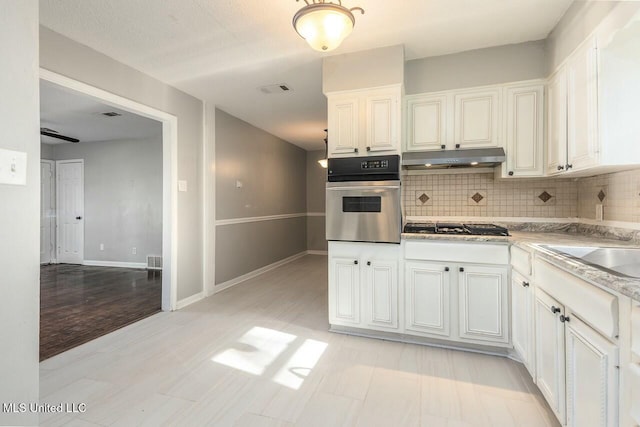 kitchen featuring oven, visible vents, gas stovetop, backsplash, and under cabinet range hood