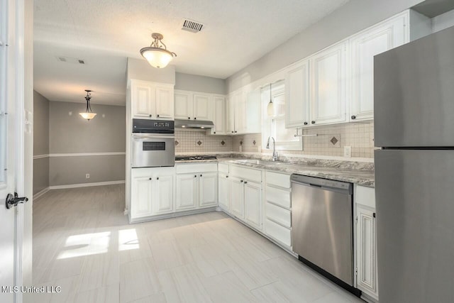 kitchen featuring stainless steel appliances, a sink, visible vents, backsplash, and under cabinet range hood
