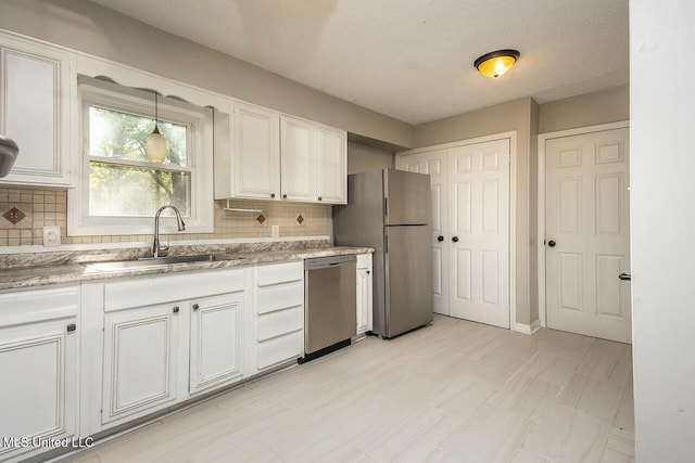 kitchen featuring white cabinets, light stone counters, stainless steel appliances, a sink, and tasteful backsplash