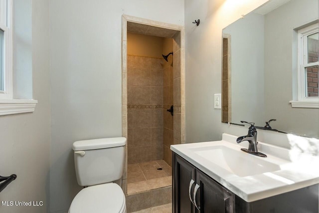 bathroom with a tile shower, toilet, and vanity