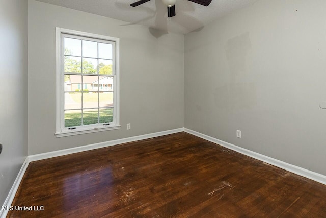 spare room featuring a ceiling fan, baseboards, a wealth of natural light, and dark wood-type flooring