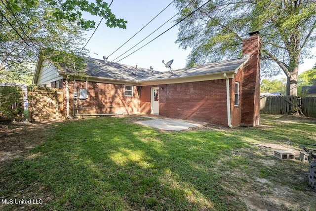 rear view of property featuring brick siding, a lawn, a chimney, and fence