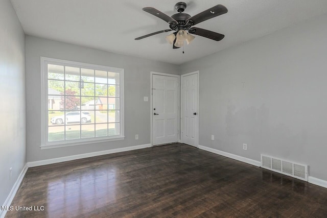 empty room featuring dark wood-type flooring, visible vents, baseboards, and ceiling fan