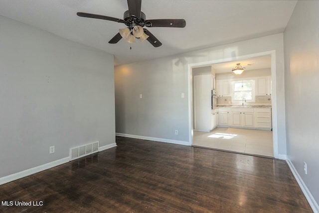 empty room featuring wood finished floors, visible vents, baseboards, and ceiling fan