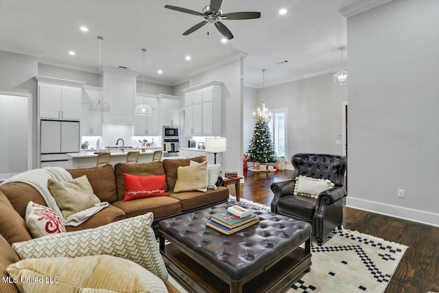 living room with ornamental molding, ceiling fan with notable chandelier, dark wood-type flooring, and sink