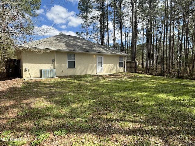 back of house with stucco siding, a lawn, fence, cooling unit, and roof with shingles