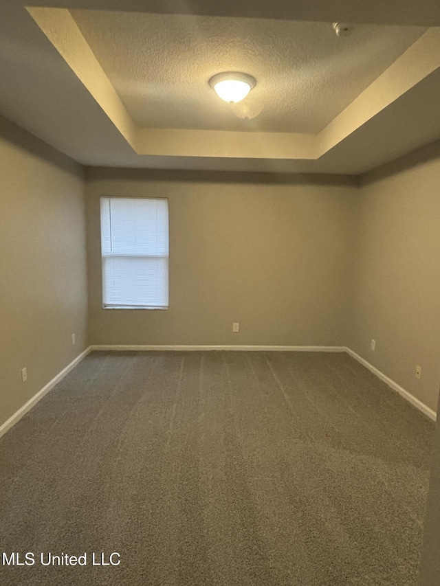 empty room featuring dark colored carpet, baseboards, a raised ceiling, and a textured ceiling