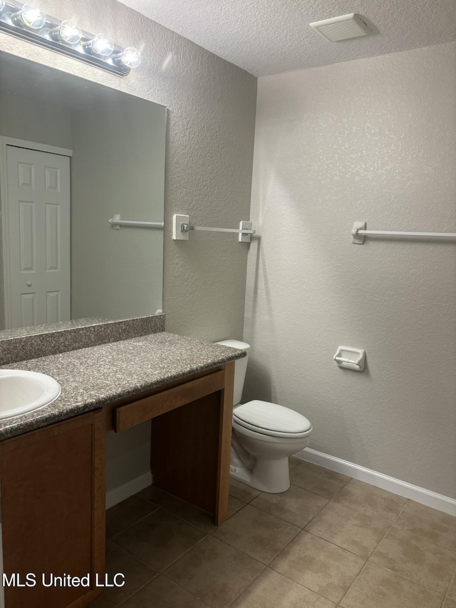 bathroom featuring tile patterned flooring, toilet, vanity, a textured wall, and a textured ceiling