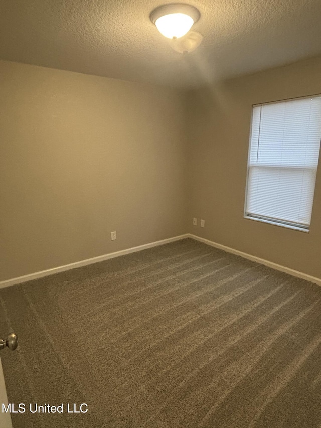 spare room with dark carpet, a textured ceiling, and baseboards