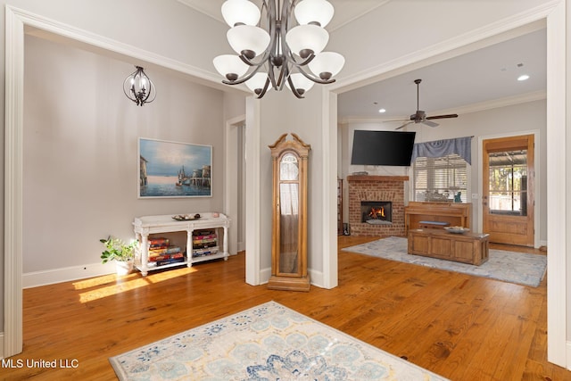 living room featuring a fireplace, ceiling fan with notable chandelier, hardwood / wood-style flooring, and ornamental molding