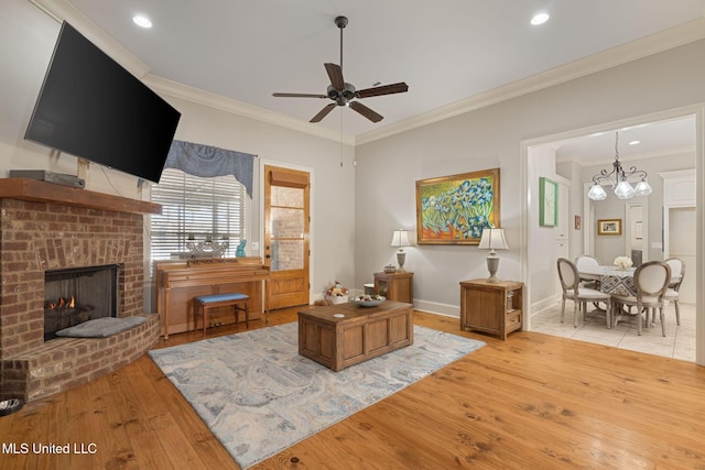 living room with a brick fireplace, ornamental molding, ceiling fan with notable chandelier, and light wood-type flooring