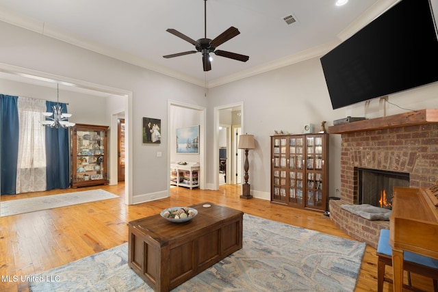 living room featuring ceiling fan with notable chandelier, light wood-type flooring, a brick fireplace, and ornamental molding