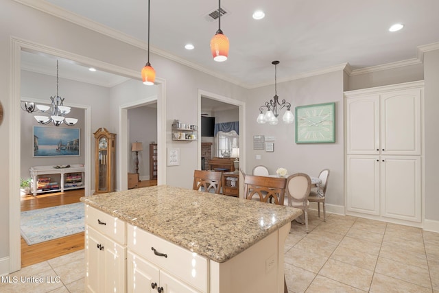 kitchen featuring a kitchen island, light stone countertops, hanging light fixtures, and light hardwood / wood-style flooring