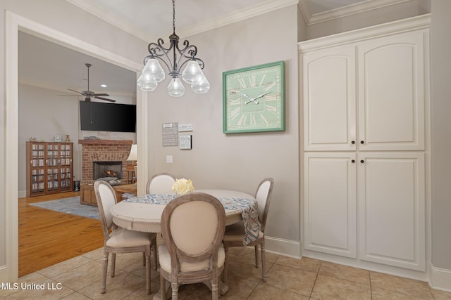 tiled dining space featuring a fireplace, ceiling fan with notable chandelier, and crown molding