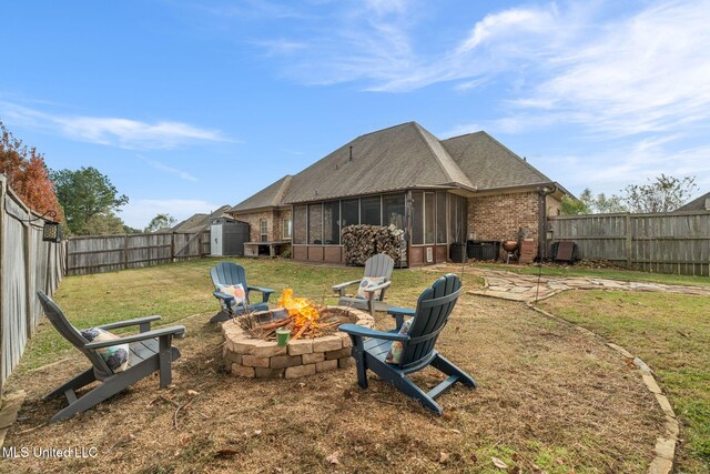 back of house with a sunroom, a yard, a fire pit, and a storage unit