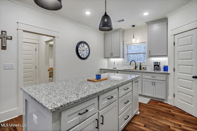 kitchen featuring decorative light fixtures, sink, backsplash, dark hardwood / wood-style floors, and a kitchen island