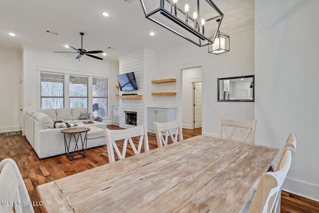 dining space with ceiling fan, a large fireplace, dark hardwood / wood-style flooring, and crown molding