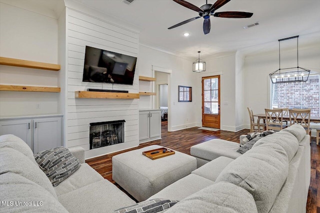 living room featuring crown molding, dark hardwood / wood-style floors, ceiling fan, and a large fireplace