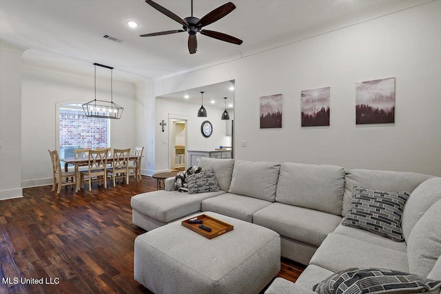 living room featuring crown molding, dark wood-type flooring, and ceiling fan with notable chandelier