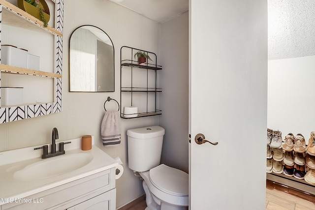 half bathroom featuring toilet, wood finished floors, and vanity