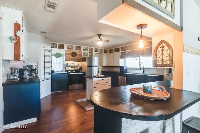 kitchen with dark countertops, visible vents, appliances with stainless steel finishes, a kitchen island, and a sink