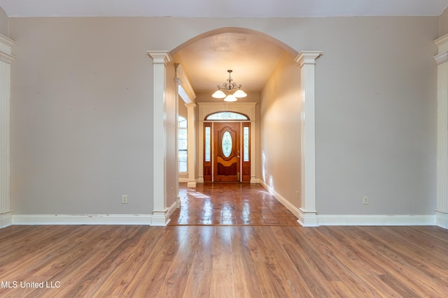 foyer featuring wood finished floors, decorative columns, arched walkways, a chandelier, and baseboards