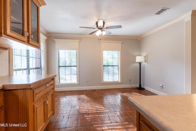 unfurnished dining area with ceiling fan, brick flooring, baseboards, and ornamental molding