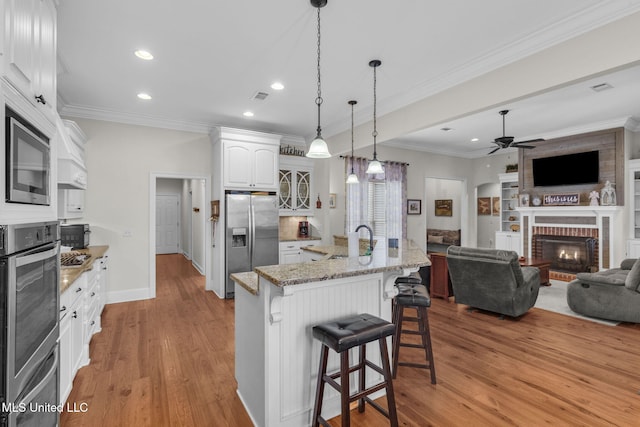 kitchen featuring sink, white cabinetry, stainless steel appliances, a kitchen breakfast bar, and light stone countertops