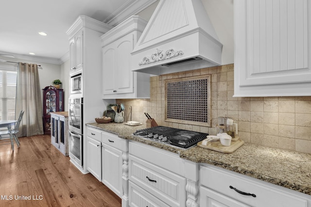 kitchen with light stone countertops, appliances with stainless steel finishes, custom range hood, and white cabinets