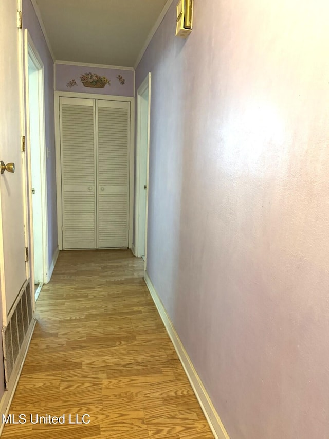 hall featuring baseboards, ornamental molding, visible vents, and light wood-type flooring