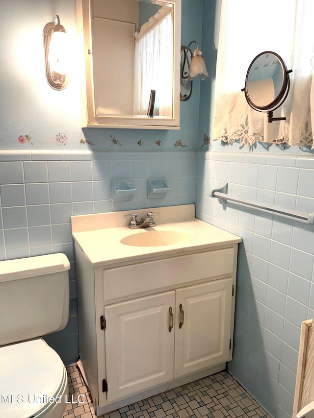 bathroom featuring a wainscoted wall, vanity, tile walls, and toilet