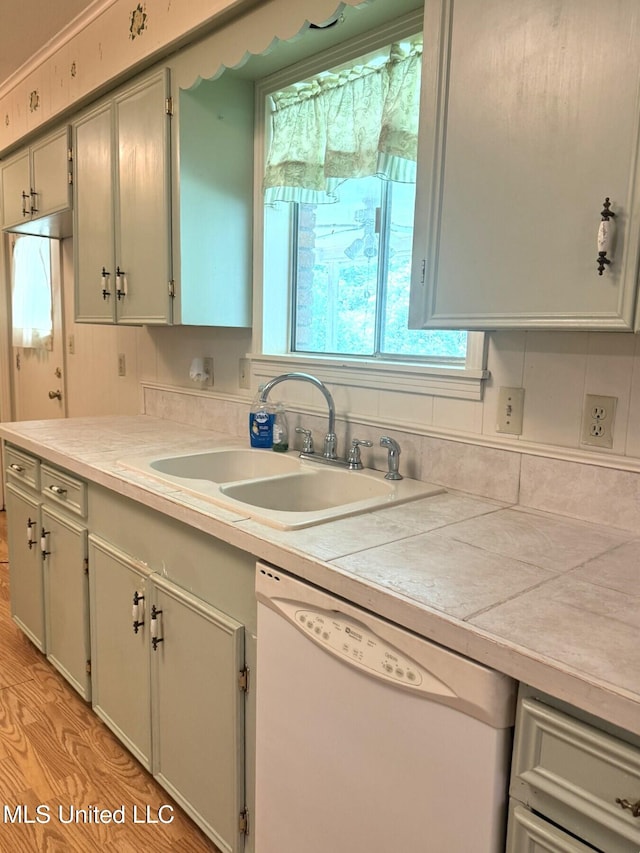 kitchen featuring white dishwasher, light countertops, light wood-type flooring, and a sink